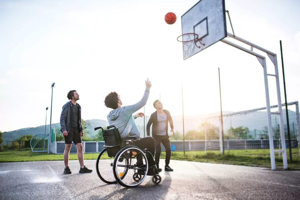 A disabled man sitting in his wheelchair and two of his friend playing basketball